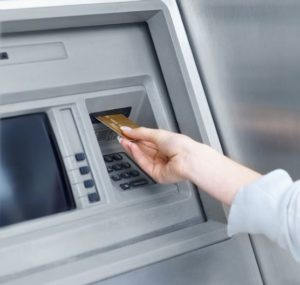 Woman pulling bank card from ATM after withdrawing stimulus check.